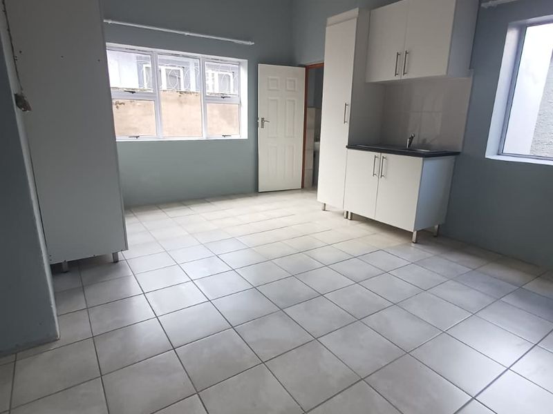 A bright, empty kitchen featuring tiled flooring, built-in white cabinetry, a sink, and large windows providing natural light.