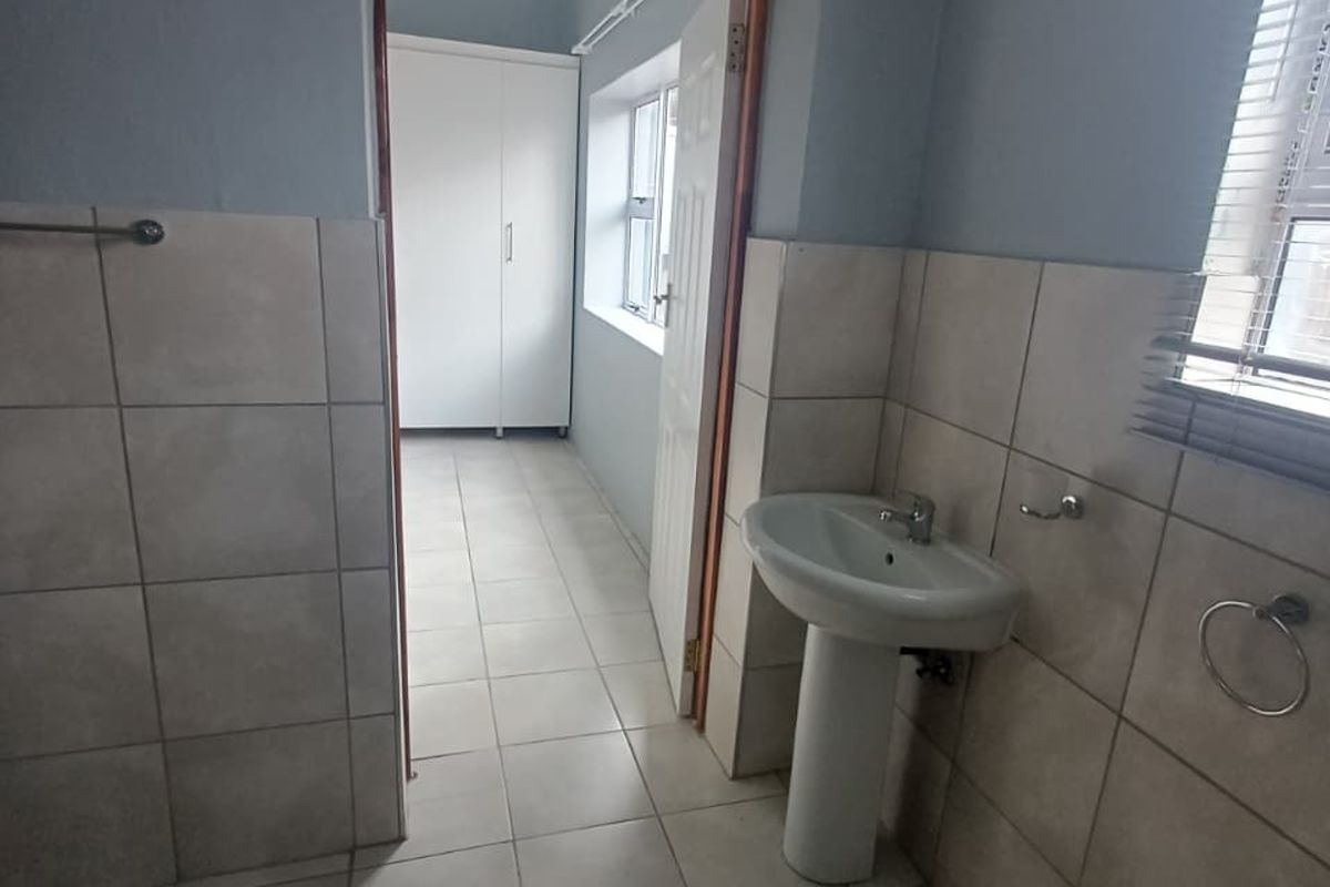 A functional bathroom featuring ceramic tiling, a pedestal basin, and a doorway leading to an adjacent room with built-in cabinetry.