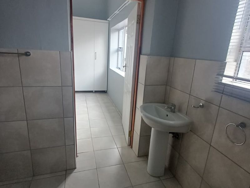 A functional bathroom featuring ceramic tiling, a pedestal basin, and a doorway leading to an adjacent room with built-in cabinetry.