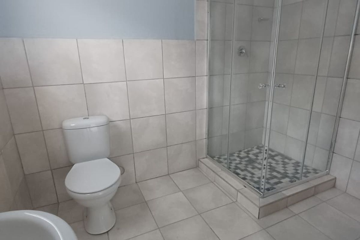 A functional bathroom featuring a glass-enclosed shower, tiled flooring, and wall tiling, presenting a clean and neutral space.