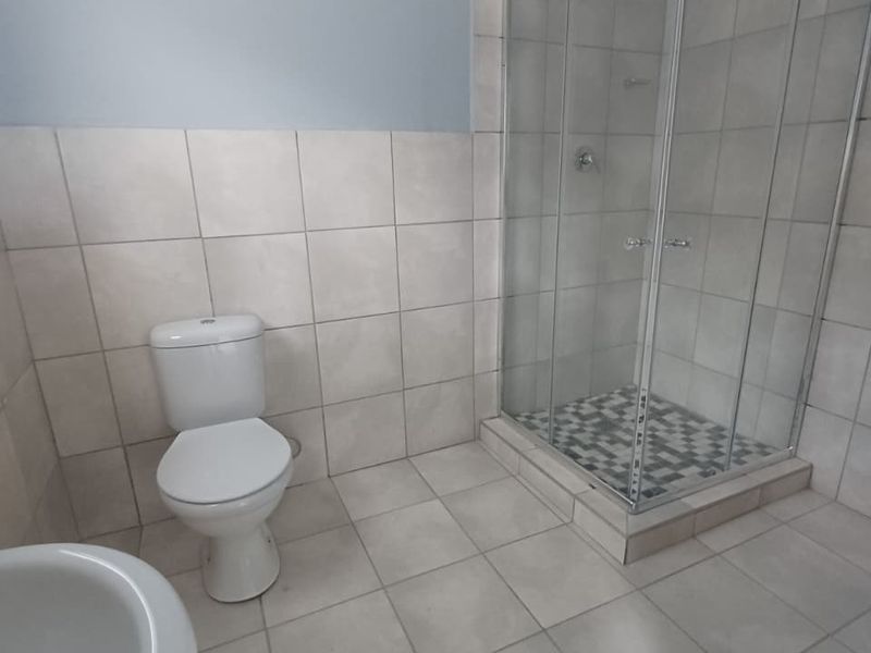A functional bathroom featuring a glass-enclosed shower, tiled flooring, and wall tiling, presenting a clean and neutral space.