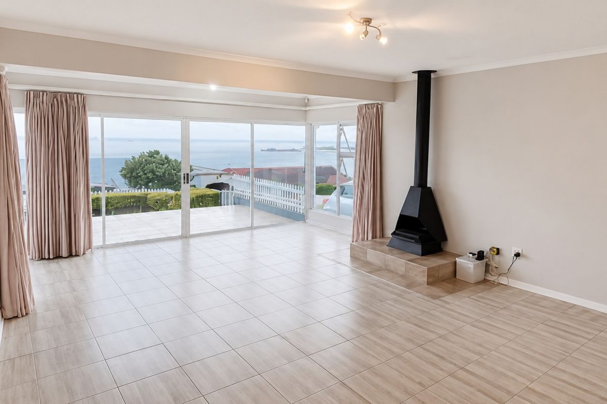 Spacious, light-filled living area featuring tiled floors, a modern freestanding fireplace, and large sliding glass doors offering expansive ocean views.