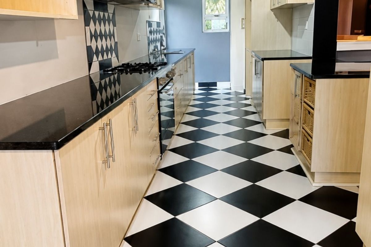 A well-maintained kitchen featuring light wood cabinetry, black granite countertops, a gas hob, and a distinctive black and white checkered tiled floor.