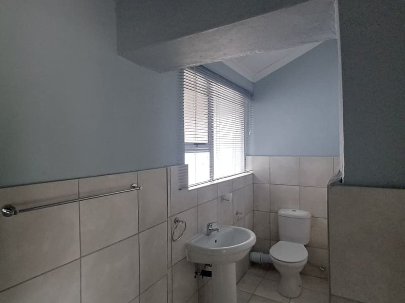 A functional bathroom featuring a pedestal basin, toilet, tiled finishes, and natural light through a window with venetian blinds.