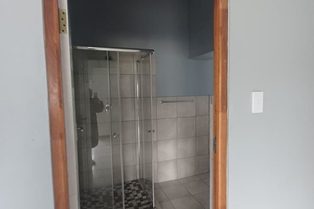 A functional bathroom featuring a glass shower enclosure, tiled flooring, and wall tiling, currently awaiting final finishing touches to the door frame.