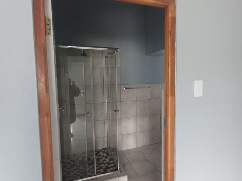 A functional bathroom featuring a glass shower enclosure, tiled flooring, and wall tiling, currently awaiting final finishing touches to the door frame.