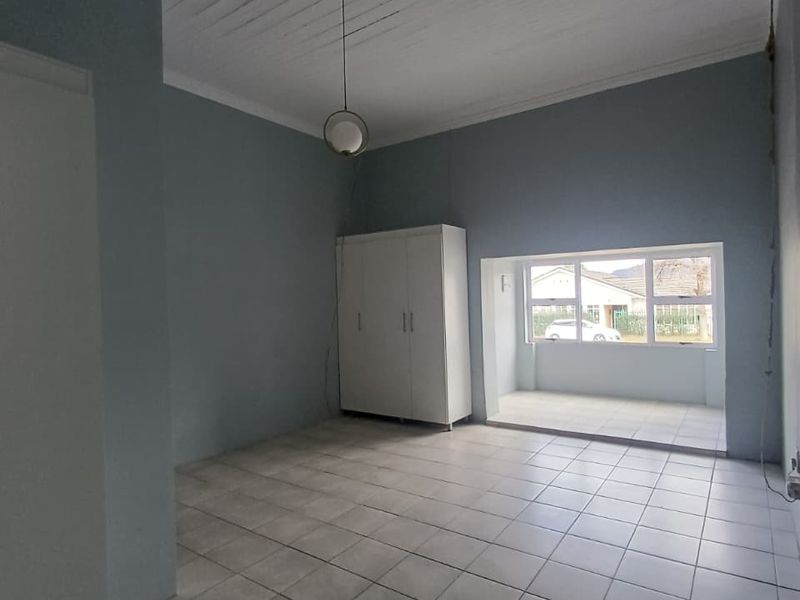 An empty bedroom featuring tiled flooring, a timber panelled ceiling, and a large window providing natural light.