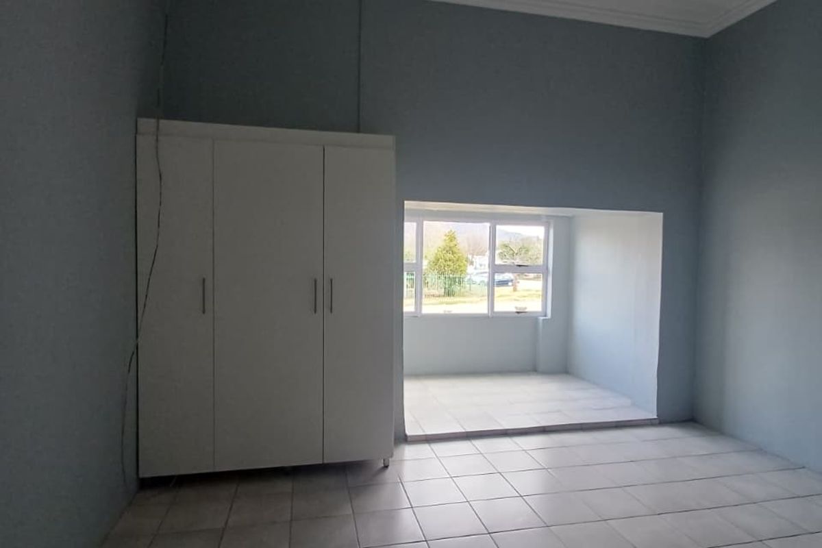 A spacious, empty bedroom featuring neutral tiled flooring, built-in wardrobe storage, and a recessed window area providing natural light.