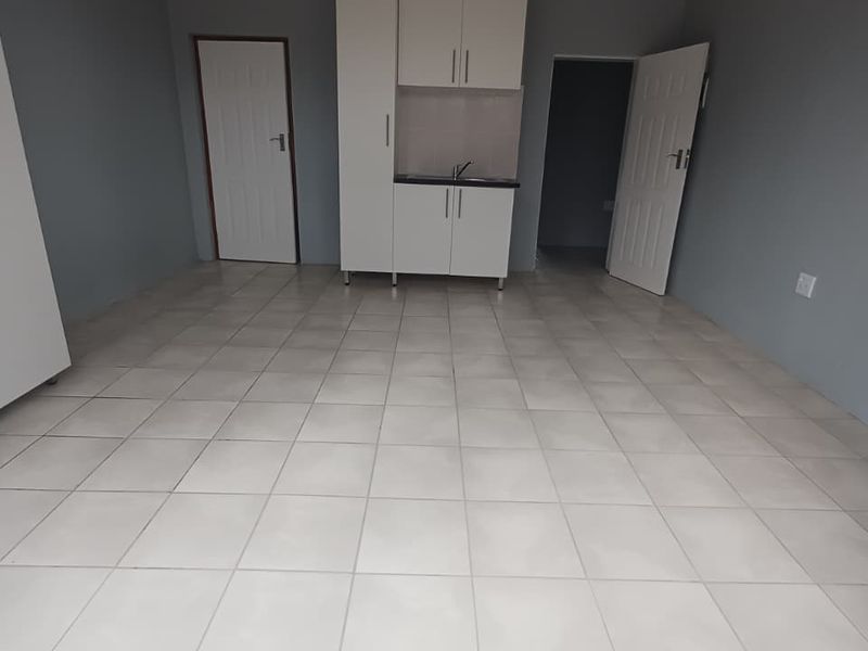 An empty kitchen area featuring white built-in cabinetry, a sink, and neutral tiled flooring, providing a clean and functional space.