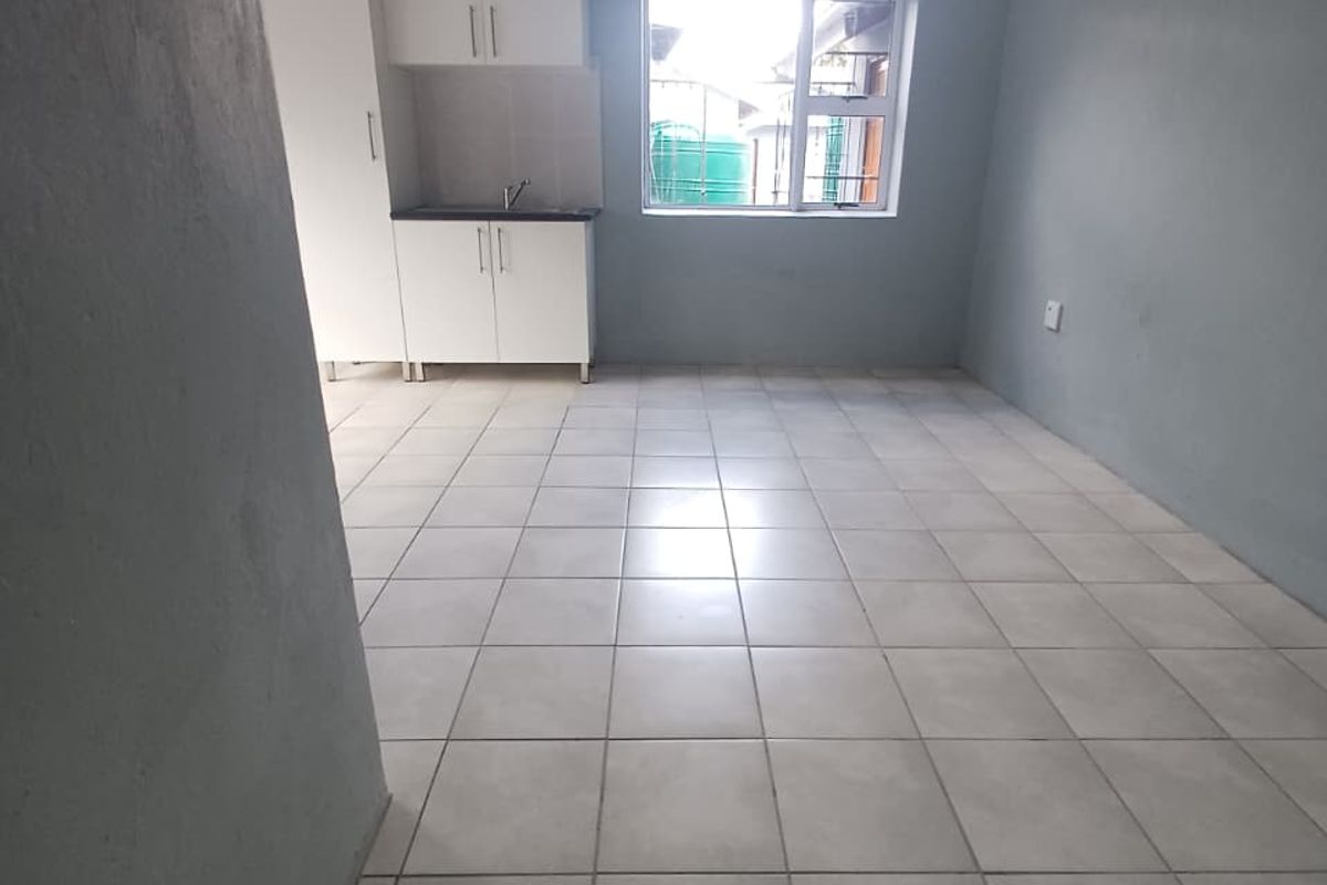 A compact, empty kitchen area featuring white cabinetry, a sink, and neutral tiled flooring, providing a clean and functional space.