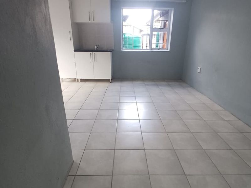 A compact, empty kitchen area featuring white cabinetry, a sink, and neutral tiled flooring, providing a clean and functional space.