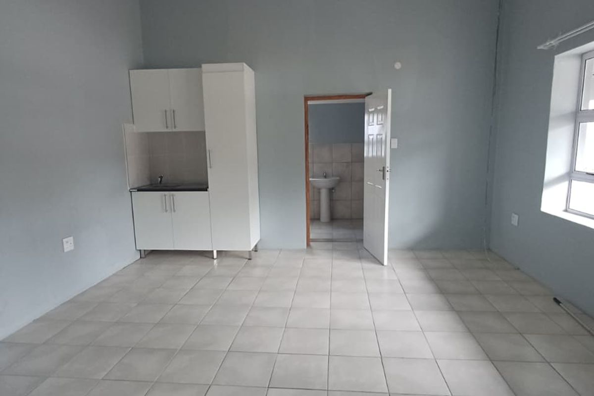 An open-plan living area featuring tiled flooring, a compact kitchenette with built-in cabinetry, and direct access to an adjoining bathroom.