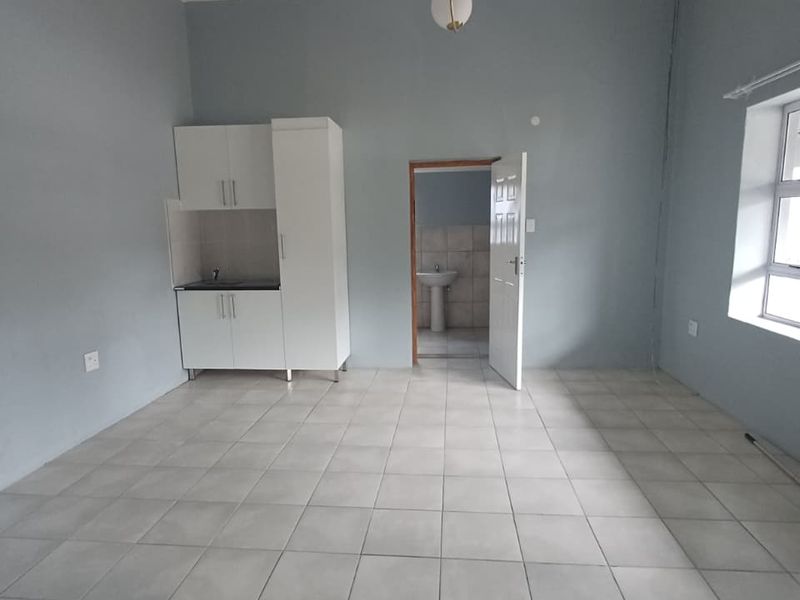 An open-plan living area featuring tiled flooring, a compact kitchenette with built-in cabinetry, and direct access to an adjoining bathroom.
