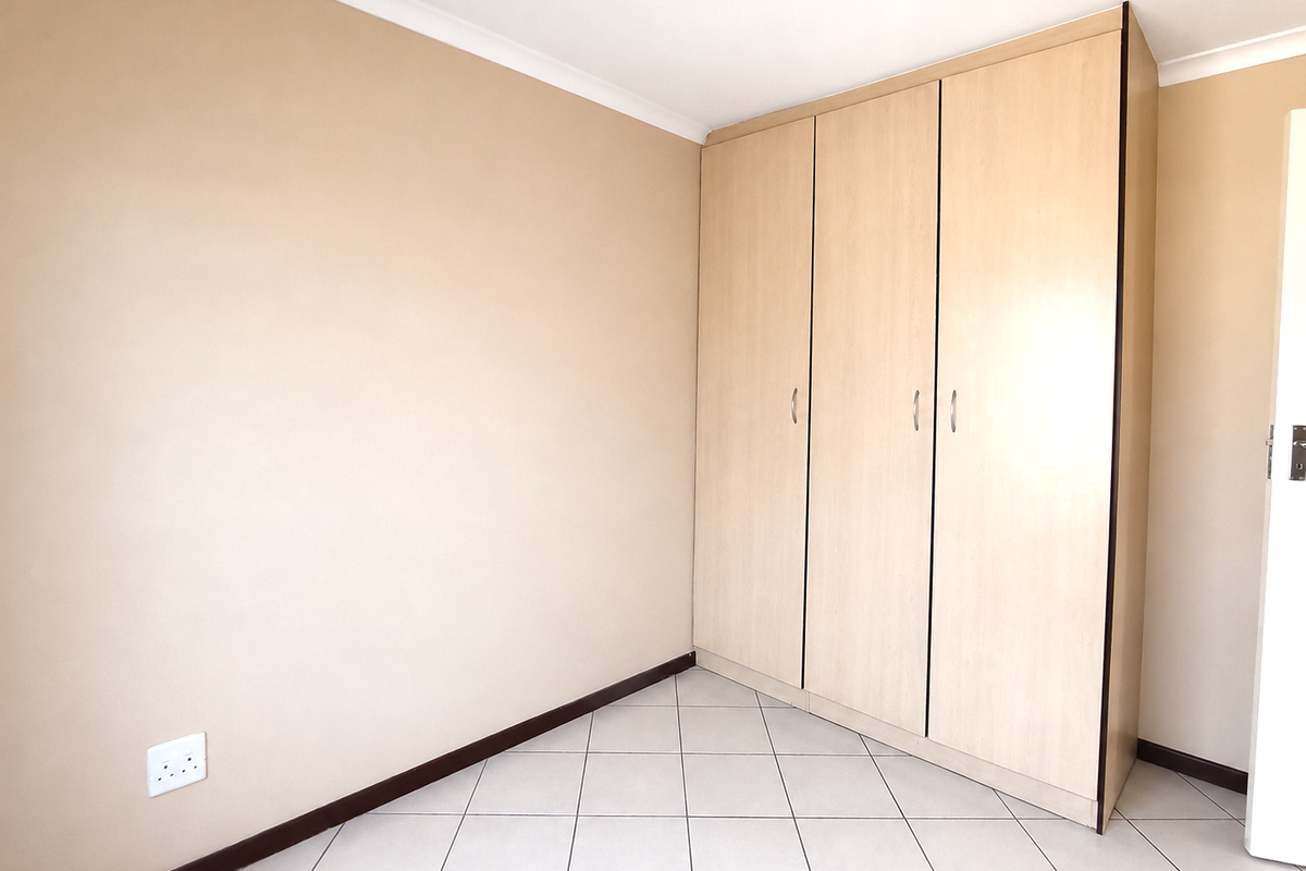 A clean, empty bedroom featuring neutral walls, tiled flooring, and a functional built-in wardrobe with light wood-finish doors.