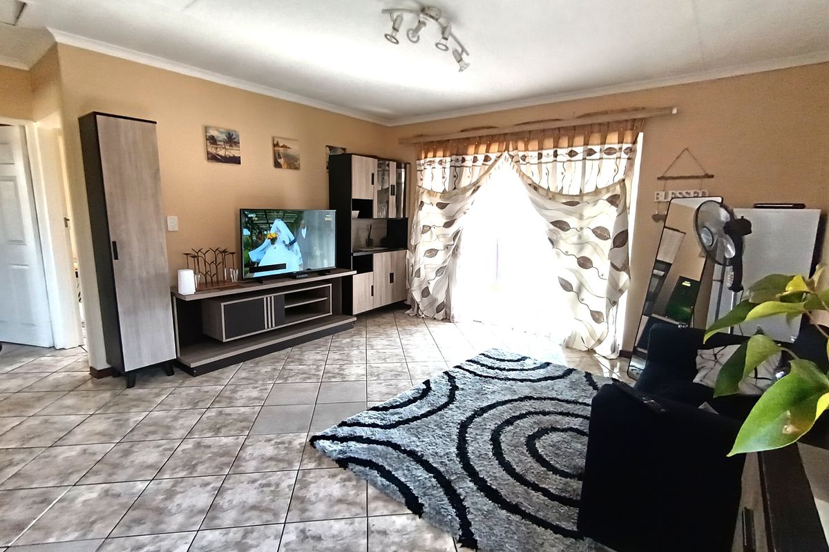 A living room featuring ceramic floor tiles, track lighting, and a sliding glass door providing natural light.