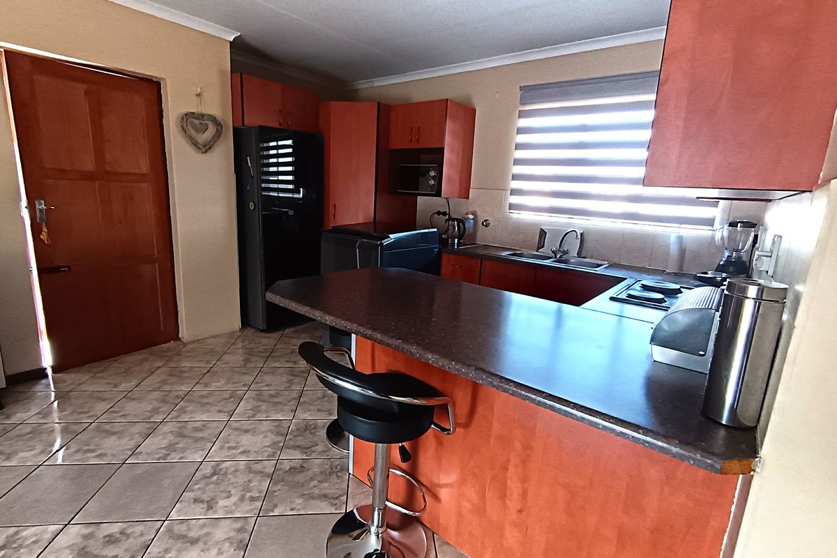 A functional kitchen featuring laminate cabinetry, dark countertops, a built-in hob, and ceramic floor tiles, offering a practical layout for daily use.