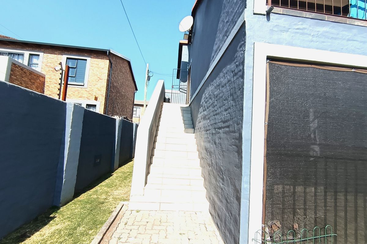 Exterior view of the property featuring a paved walkway, boundary wall, and an external staircase leading to the upper level.