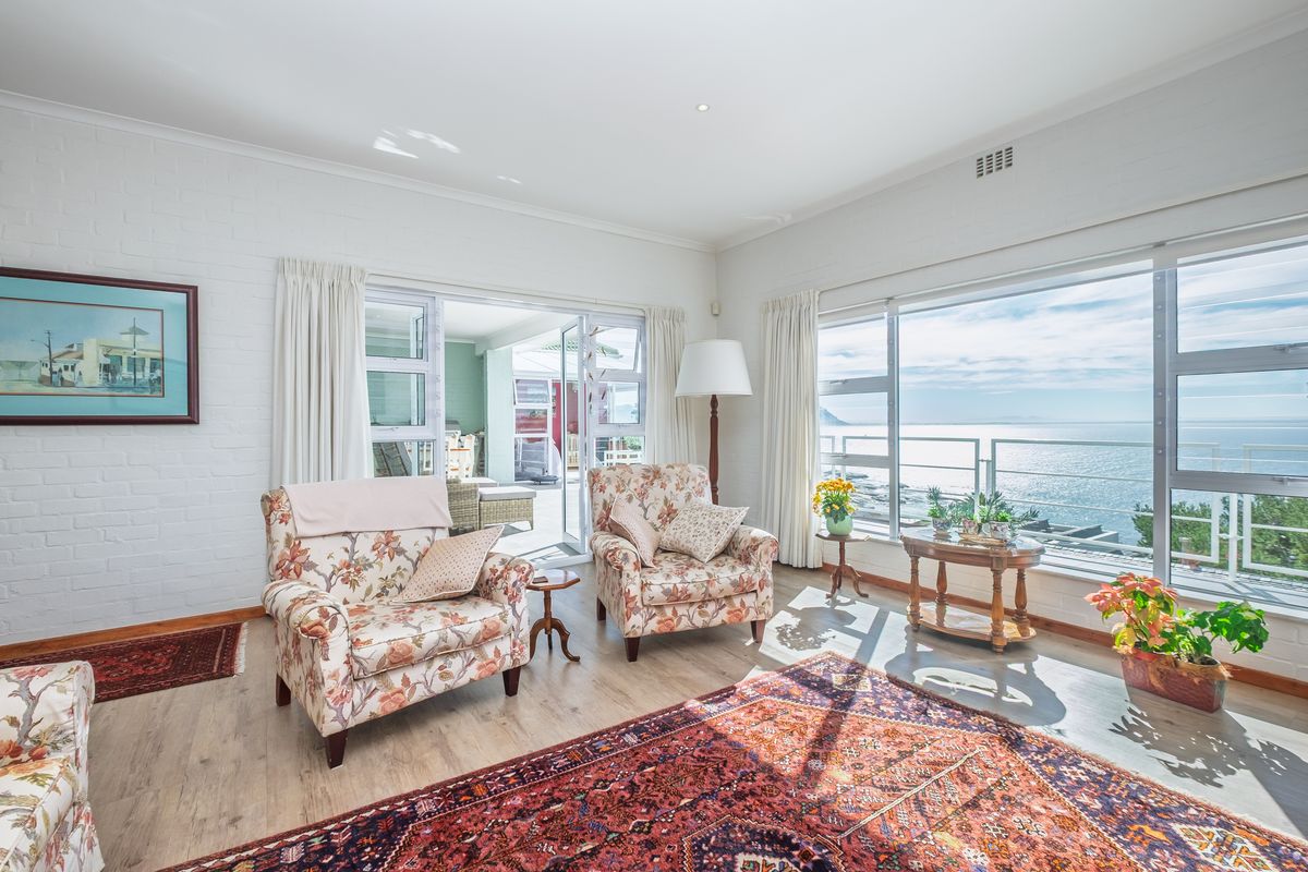 Bright living room featuring painted brick walls, laminate flooring, and large windows offering expansive ocean views with direct access to an outdoor patio area.