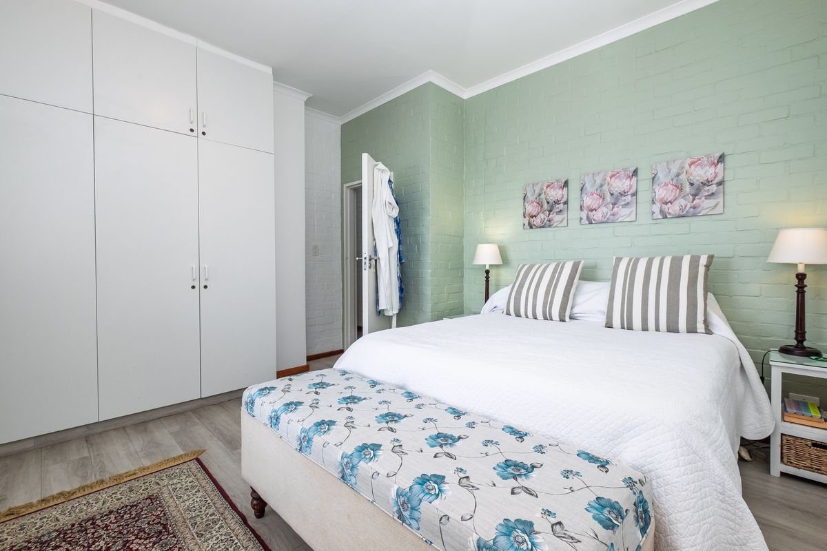 A well-maintained bedroom featuring a painted brick accent wall, built-in storage cupboards, and light-toned laminate flooring.