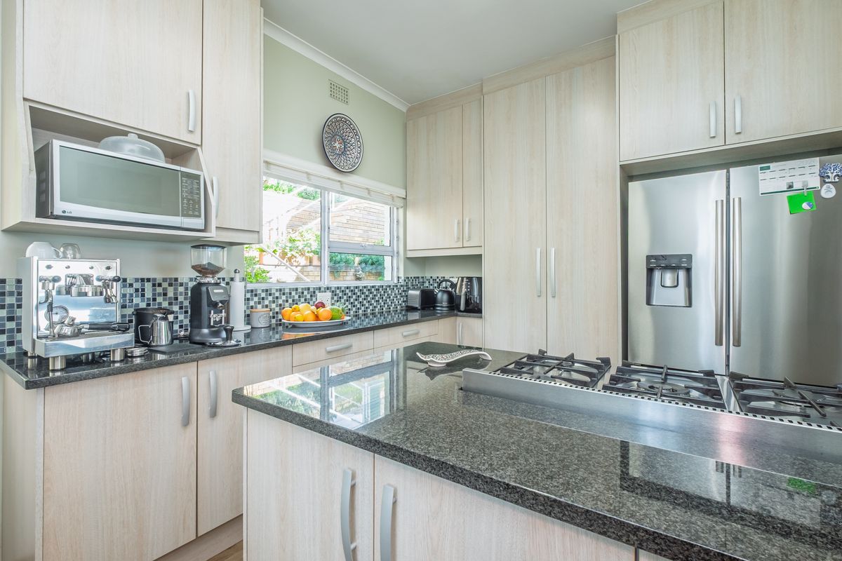 Modern kitchen featuring light wood cabinetry, dark granite countertops, a mosaic tile backsplash, and integrated stainless steel appliances.