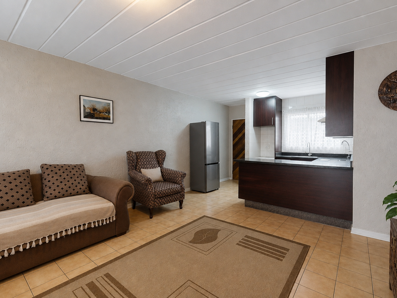 Open-plan living area featuring a compact kitchen with dark cabinetry, stone countertops, and tiled flooring throughout the combined space.