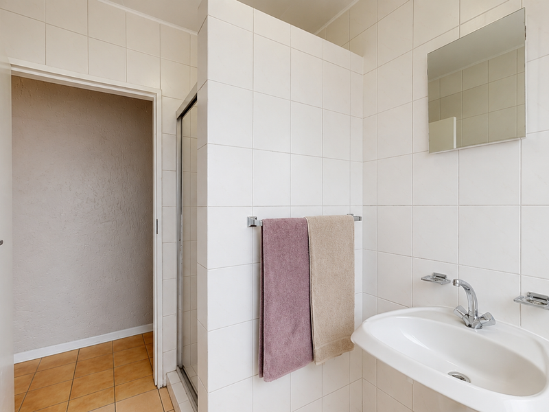 A functional bathroom featuring white wall tiles, a wall-mounted basin with chrome fixtures, and a separate shower enclosure.