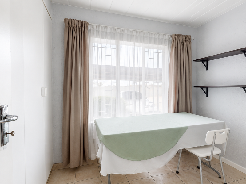 A functional bedroom featuring tiled flooring, built-in cupboard storage, and security bars on the window for added peace of mind.