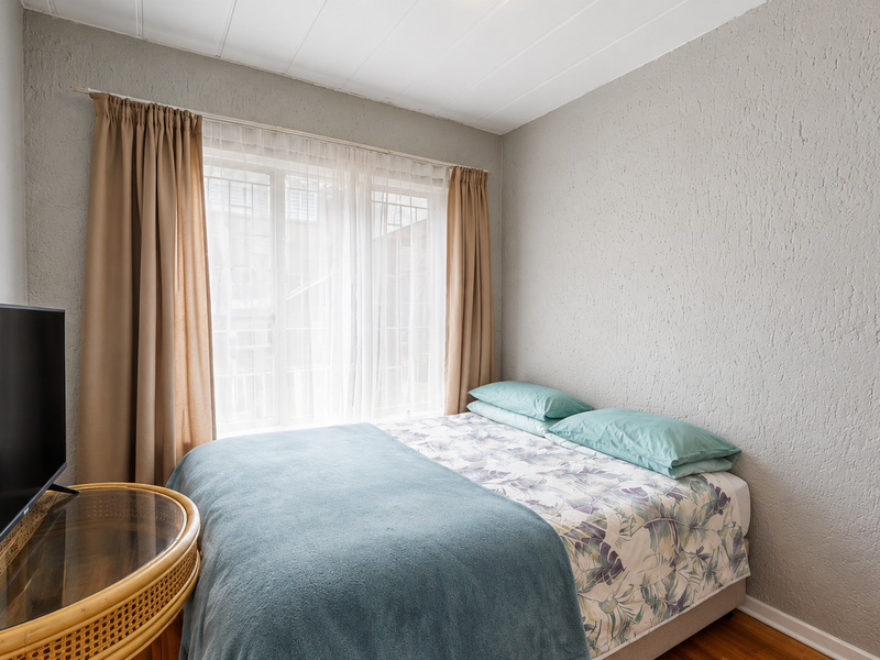A cozy bedroom featuring textured walls, timber flooring, and a large window with curtains, providing a comfortable and functional sleeping space.