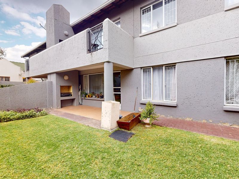 Rear exterior view of the townhouse featuring a covered patio with a built-in braai, balcony, and a private garden area.