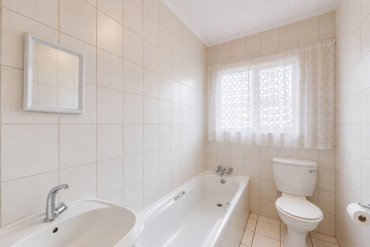 A clean, functional bathroom featuring a bathtub, toilet, and washbasin with neutral wall and floor tiling.