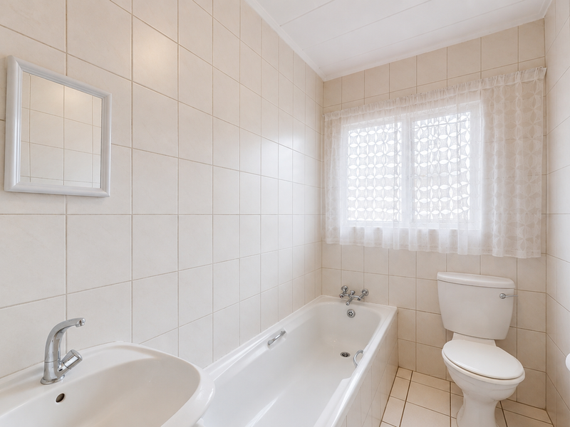 A clean, functional bathroom featuring a bathtub, toilet, and washbasin with neutral wall and floor tiling.