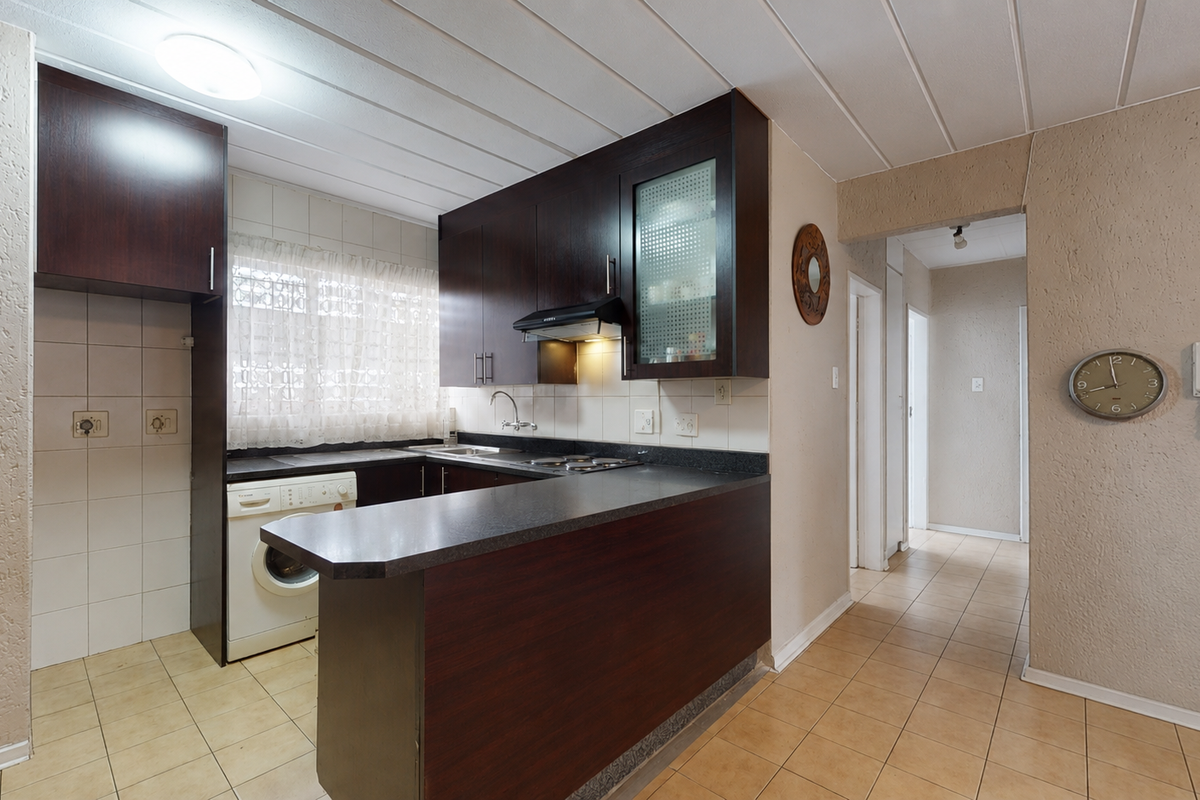 A functional kitchen featuring dark wood cabinetry, laminate countertops, tiled backsplash, and ceramic floor tiles, offering a practical layout for daily use.