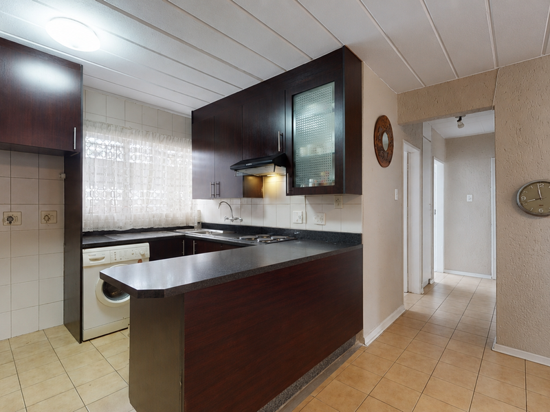 A functional kitchen featuring dark wood cabinetry, laminate countertops, tiled backsplash, and ceramic floor tiles, offering a practical layout for daily use.