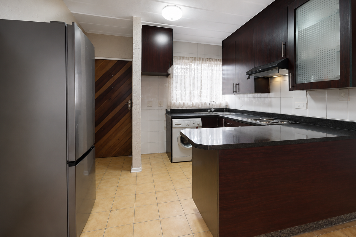 Functional kitchen featuring dark wood cabinetry, granite countertops, tiled backsplash, and integrated hob, offering a practical layout for daily meal preparation.