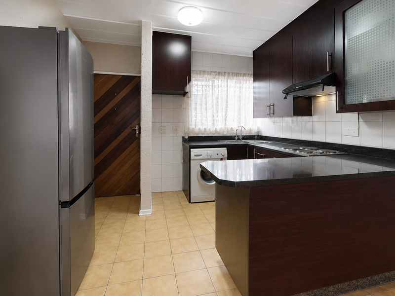 Functional kitchen featuring dark wood cabinetry, granite countertops, tiled backsplash, and integrated hob, offering a practical layout for daily meal preparation.