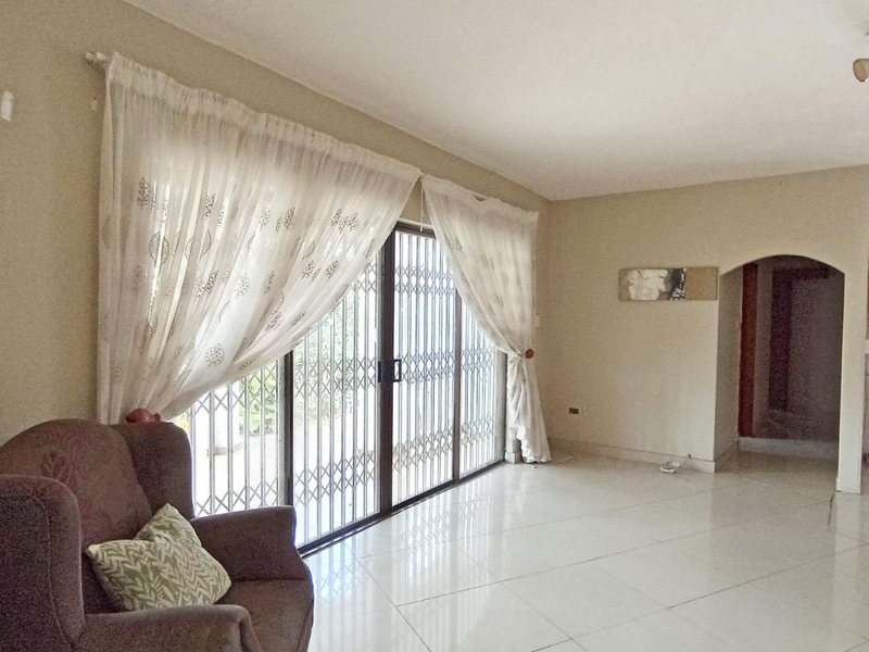 Spacious living area featuring large sliding glass doors with security gates, neutral tiled flooring, and an arched entryway leading to adjacent spaces.