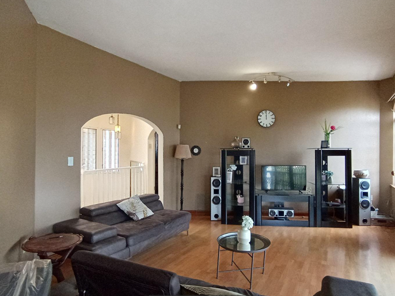 Spacious living room featuring laminate flooring, an arched entryway, and large sliding glass doors with security gates providing access to the exterior.