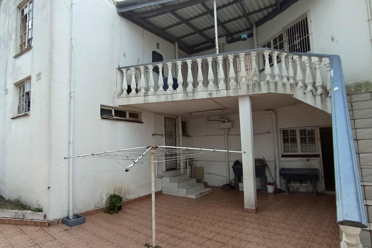 Rear exterior view featuring a covered patio area, an elevated balcony with balustrades, and an external staircase leading to the upper level.