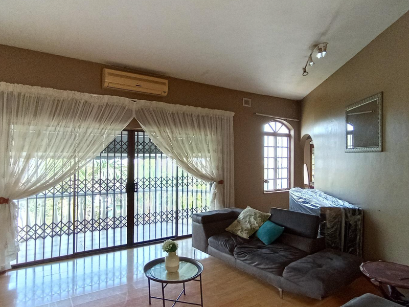Spacious living room featuring tiled flooring, a split-system air conditioner, and large sliding glass doors with security gates leading to an outdoor area.