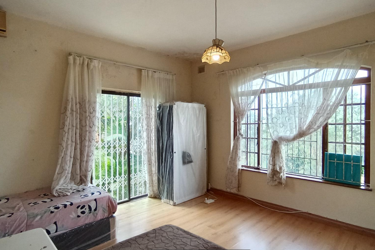 A bedroom featuring laminate flooring, built-in cupboards, an air conditioning unit, and large windows with security bars, requiring some cosmetic updates.