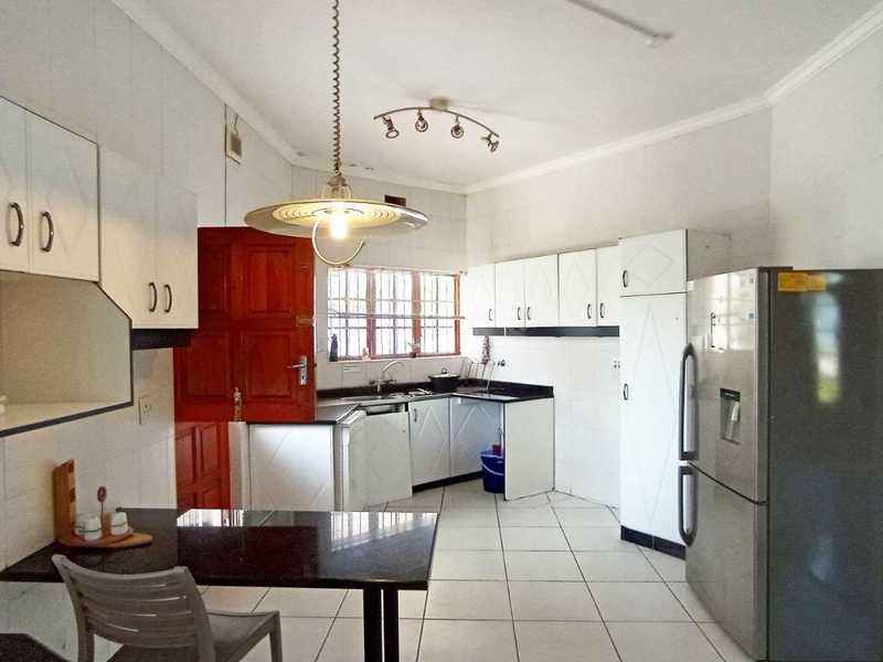 A functional kitchen featuring white built-in cabinetry, dark granite countertops, tiled flooring, and a breakfast nook area.