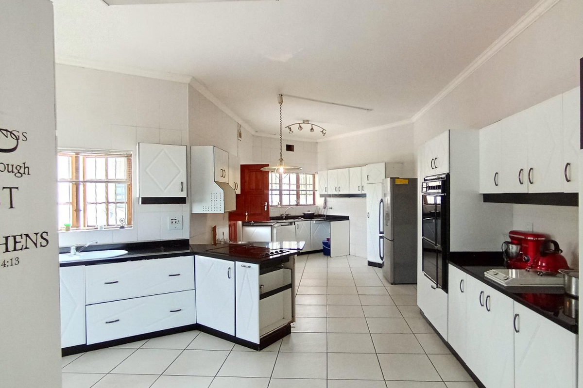 Spacious kitchen featuring white built-in cabinetry, dark granite countertops, tiled flooring, and integrated oven and hob.