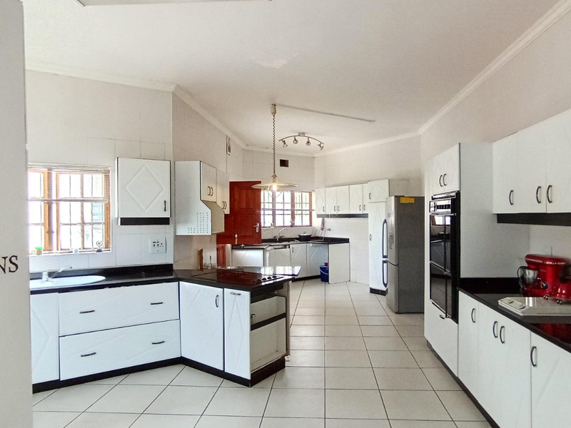 Spacious kitchen featuring white built-in cabinetry, dark granite countertops, tiled flooring, and integrated oven and hob.