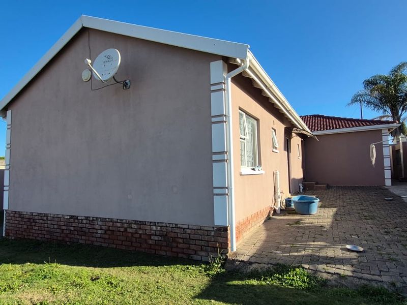 Rear view of the property featuring plastered walls, brick plinth, and paved outdoor area with a satellite dish mounted on the side elevation.