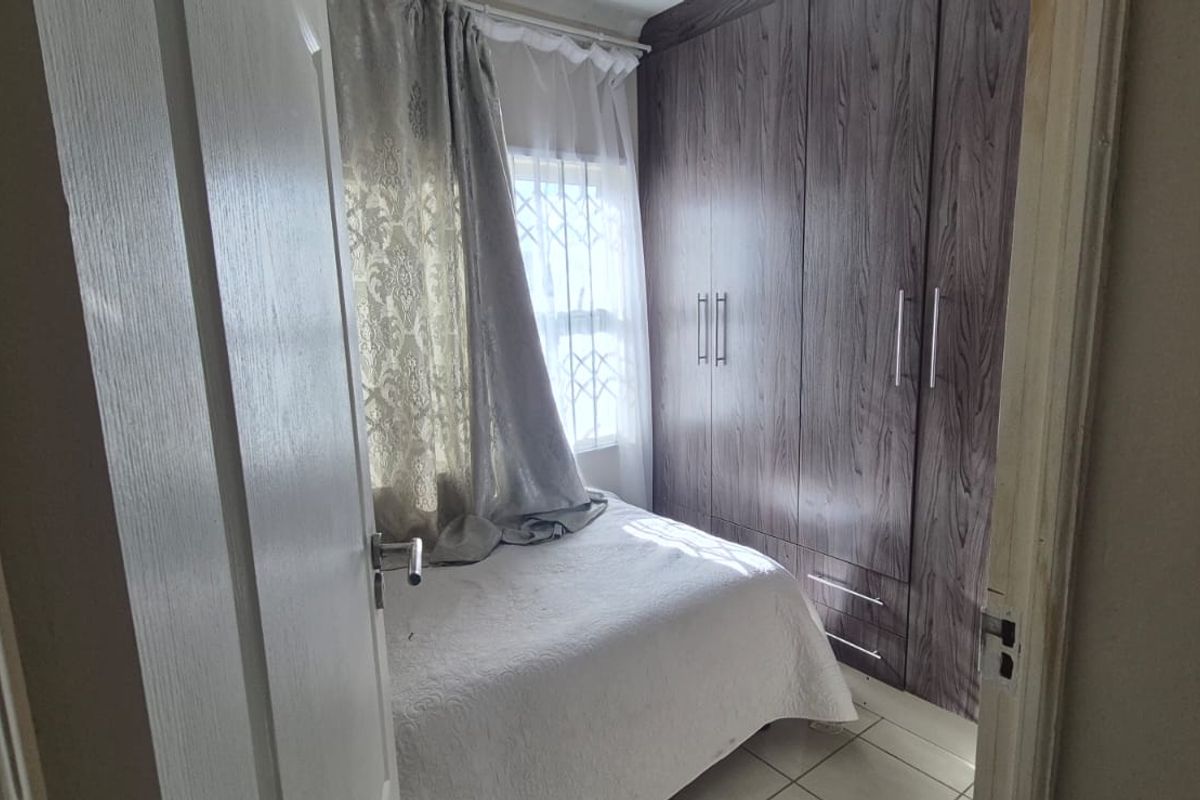 A compact bedroom featuring built-in wooden cupboards, tiled flooring, and a window fitted with a security gate.