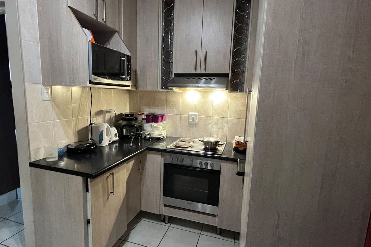 Compact kitchen featuring light wood-finish cabinetry, dark countertops, tiled backsplash, and integrated appliances including an oven, hob, and extractor fan.