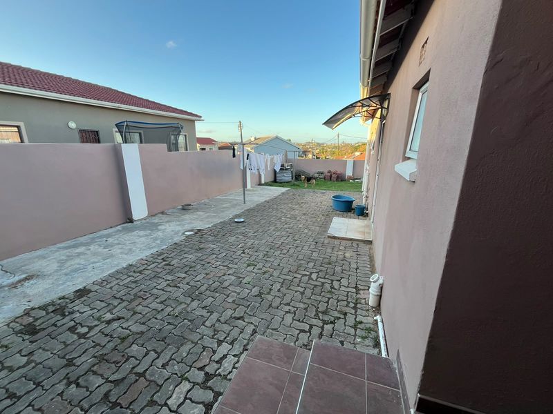 A rear exterior area featuring paved flooring, a boundary wall, and a small awning over the entrance, providing a functional outdoor space.