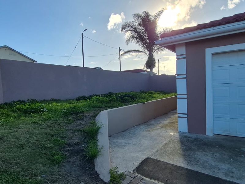 Rear exterior view showing a garage, concrete pathway, and perimeter wall with an adjacent lawn area.