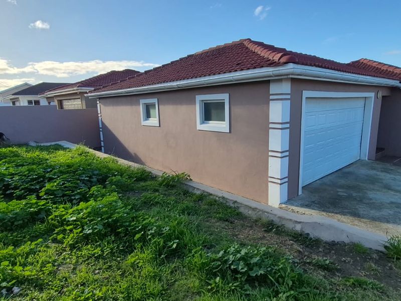 Rear view of the property featuring a tiled roof, garage access, and a large garden area requiring landscaping.