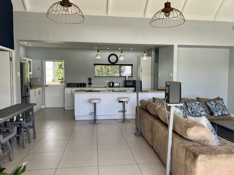 Spacious open-plan living and kitchen area featuring a central island, tiled flooring, vaulted ceilings, and modern pendant lighting.